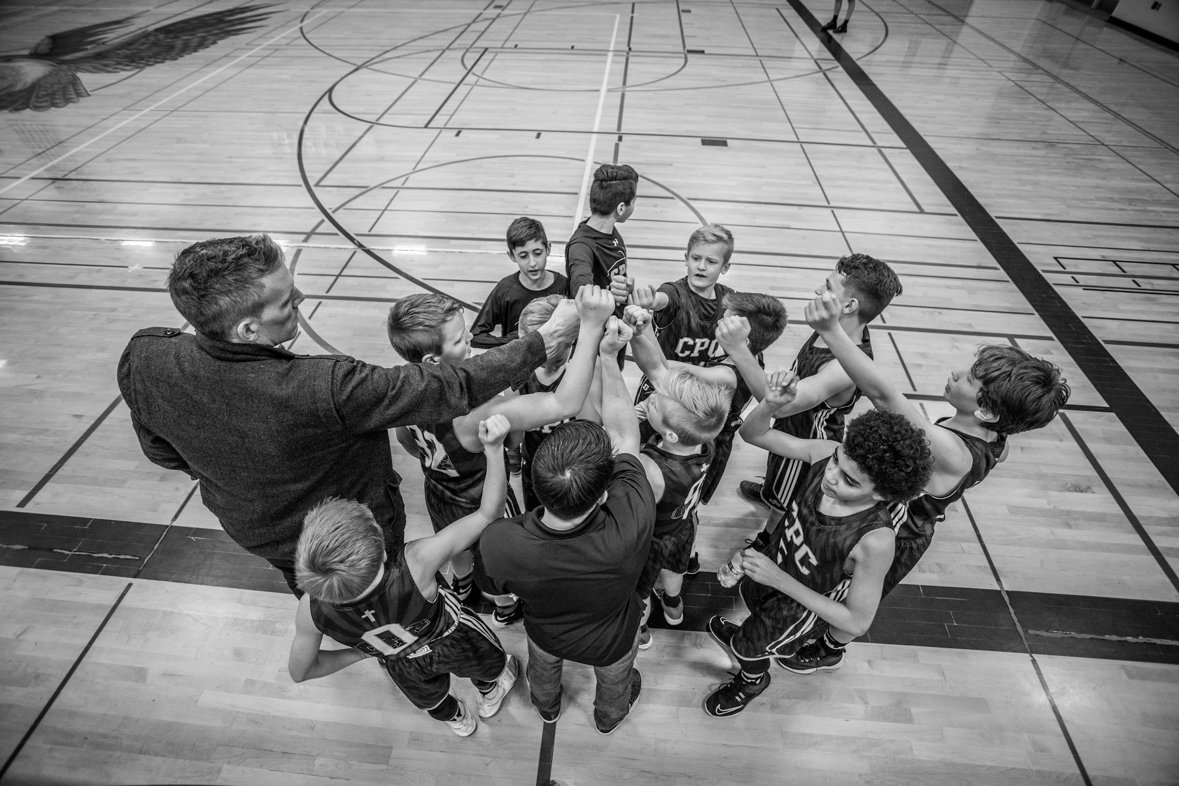Coach and children with arms up in a huddle